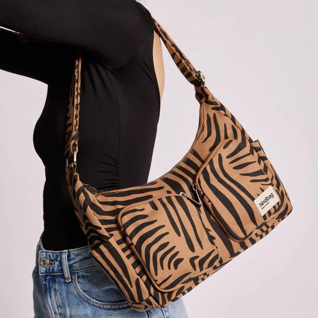Bolso Emile de la marca Hindbag en estampado cebra color canela de fondo, mostrando sus varios bolsillos delanteros sujetado por una persona