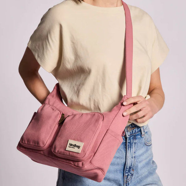 Bolso del modelo Emile de la marca Hindbag en color rosa con bolsillos y el logo de Hindbag en uno de ellos, sujetado por las manos de una persona