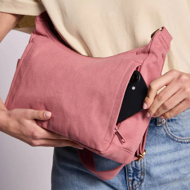 Bolso del modelo Emile de la marca Hindbag en color rosa donde se ve una persona metiendo un móvil inteligente dentro de uno de los bolsillos traseros del bolso. 