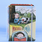 Portada de agenda semanal 2027 Macanudo de Liniers con Enriqueta leyendo bajo un árbol, tapa dura con elástico de cierre