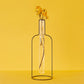 Florero con forma de silueta de botella de hierro con una probeta de cristal que contiene un tallo de flores secas con el fondo amarillo
