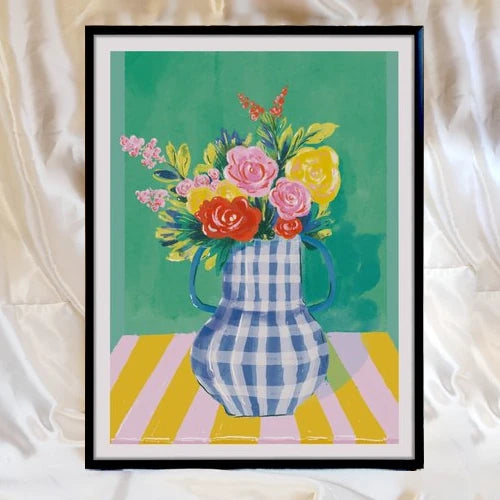 lámina de Laura Ortiz de un florero en colores azul y blanco sobre una mesa con mantel de rayas blancas y amarillas, y con flores variadas sobre una pared verde, y emarcado en un cuadro negro