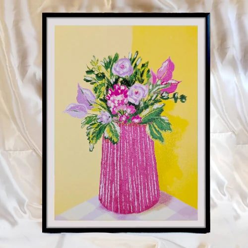 lámina de Laura Ortiz de un florero en color rosa fucsia sobre una mesa con mantel de cuadros blancos y lilas, y con flores variadas sobre una pared en esquina de color amarillo, y emarcado en un cuadro negro