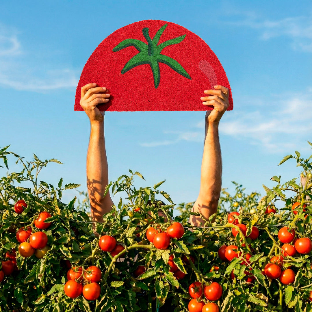Persona entre matas de tomate sujetando un felpudo con forma de medio tomate por encima de la cabeza con un cielo azul de fondo