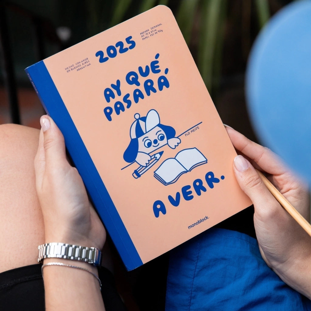 Manos de mujer con la agenda 2025 de la ilustradora argentina Flo Meije a semana vista con un perrito que va a escribir en una libreta en blanco y el mensaje "ay qué pasará a verr"