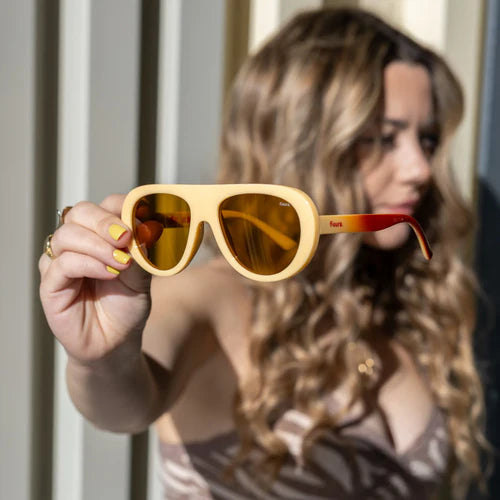 Mujer sujetando unas gafas de sol de montura amarillo vainilla y patillas con degradado