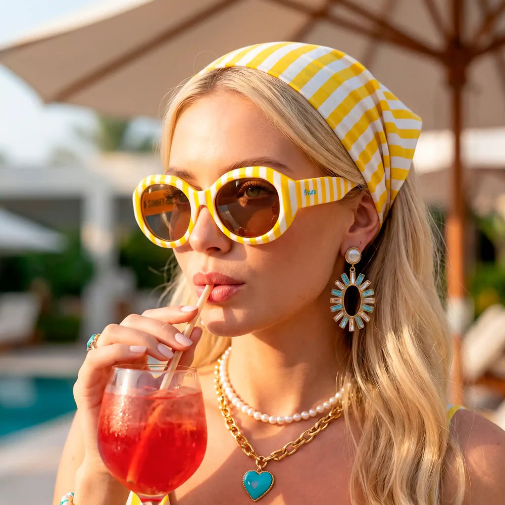 Mujer con pañuelo en la cabeza y gafas de sol a rayas amarillas y blancas bebiendo aperol con una pajita