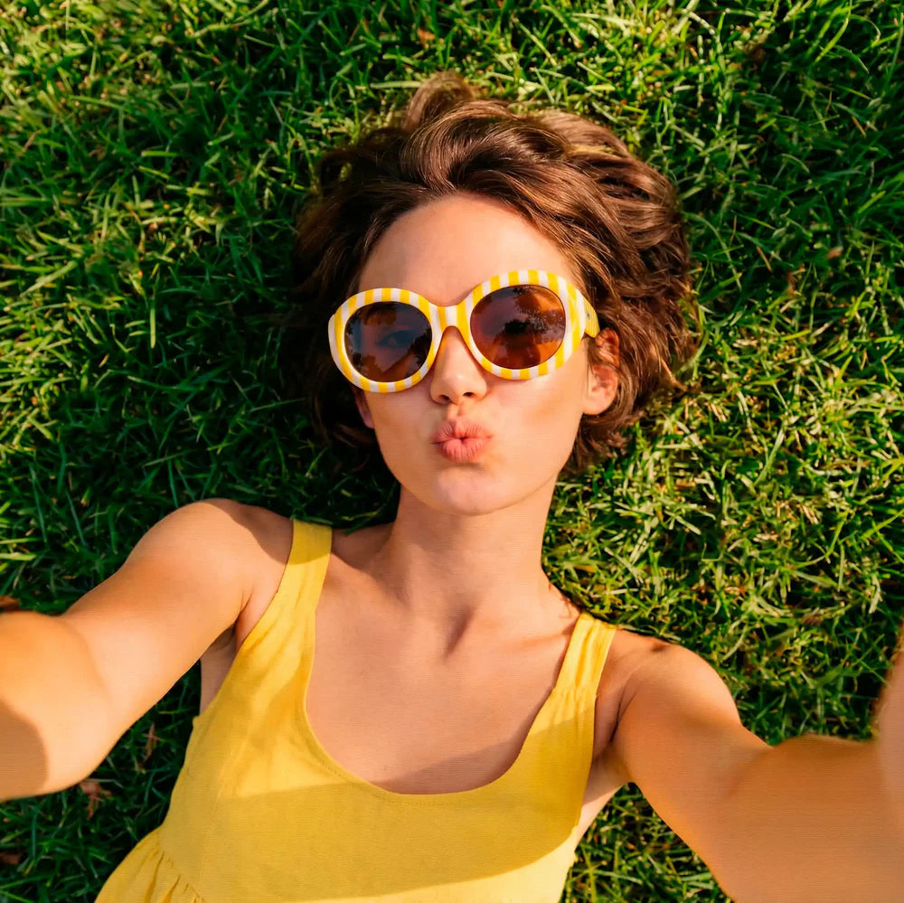 Chica con camiseta amarilla y gafas de sol con montura a rayas amarillas y blancas tumbada en el césped