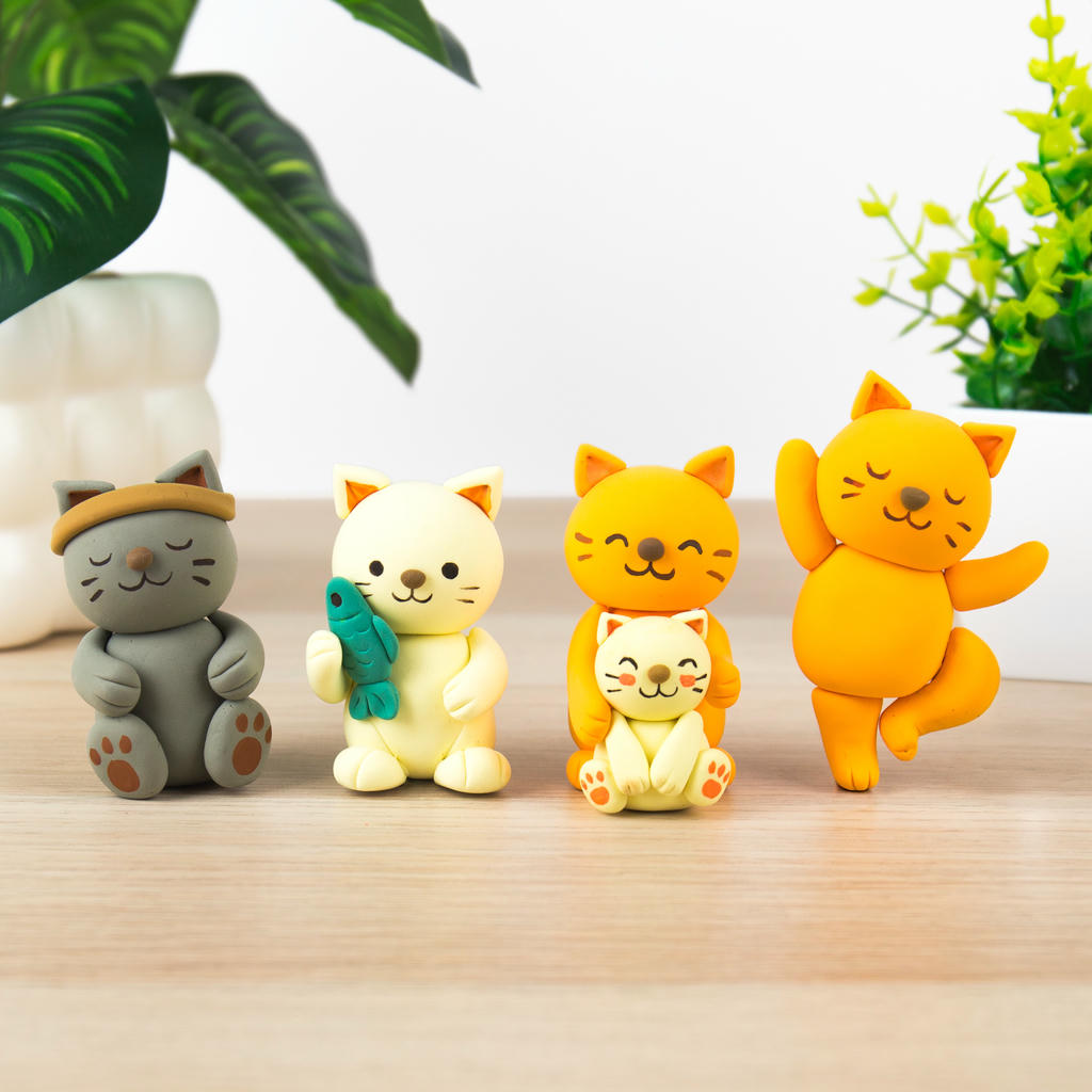 Cinco gatos modelados con el Kit DIY Gatos: uno gris, uno claro con un pez, una pareja de gato y gatito y uno naranja con las patas levantadas.