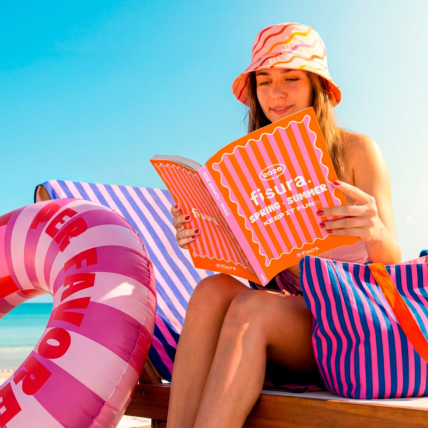 Chica en la plaa leyendo el catálogo de Fisura con un gorro de pescador a ondas de colores
