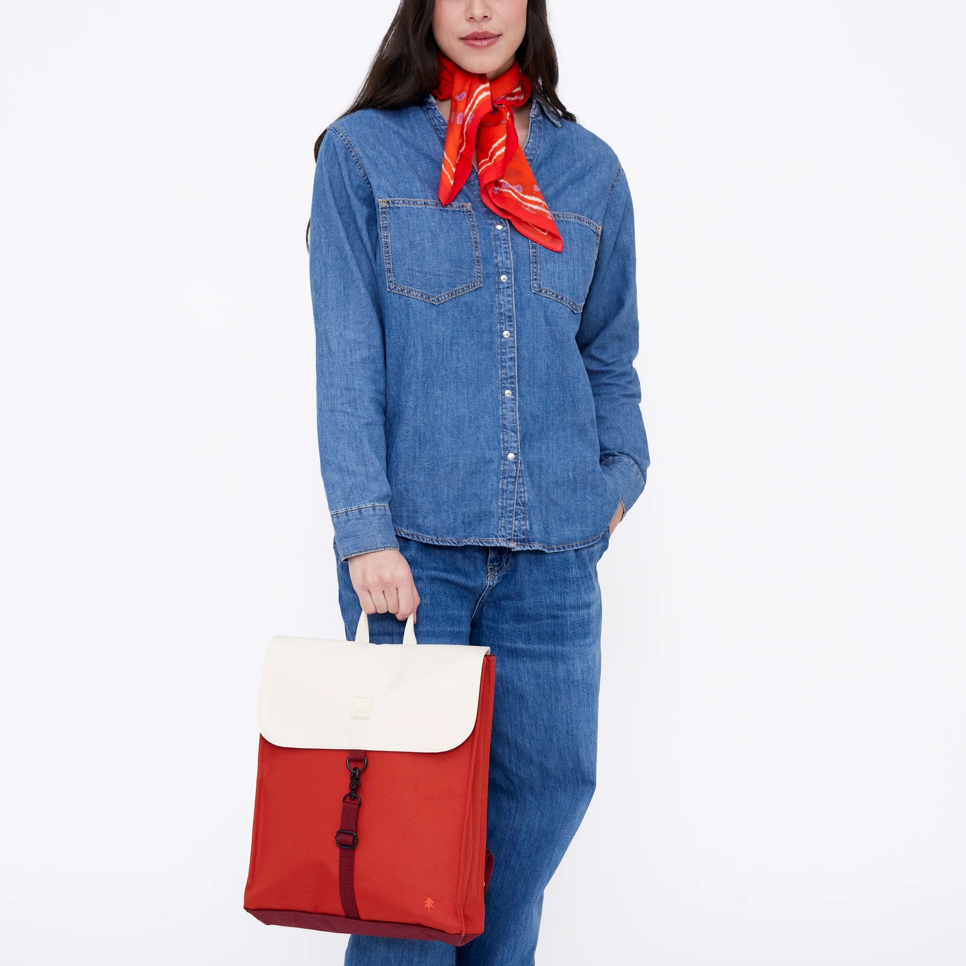 Mujer vestida con camisa y pantalón vaquero con pañuelo rojo al cuello y la mochila reciclada e impermeable blanca y cereza de Lefrik