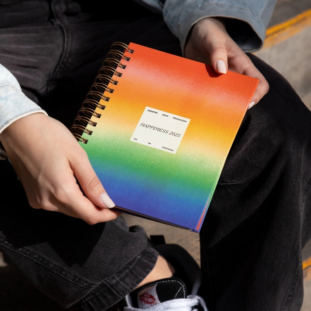 Mujer sentada con la agenda 2025 Happimess Primavera con portada a franjas de colores y organización a semana vista