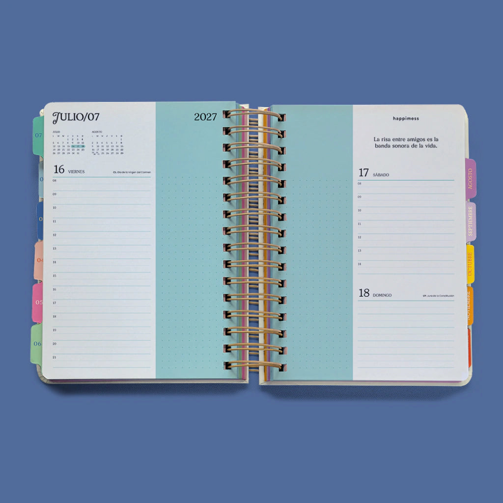 Interior de la agenda diaria 2027 Happimess abierta mostrando páginas de julio con separadores mensuales de colores, franja turquesa central y frase motivacional en la página derecha