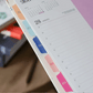 Lomo de la agenda diaria 2027 Happimess con separadores mensuales de colores numerados del 01 al 05 en tonos naranja, azul, azul marino, rosa y fucsia, con páginas diarias visibles