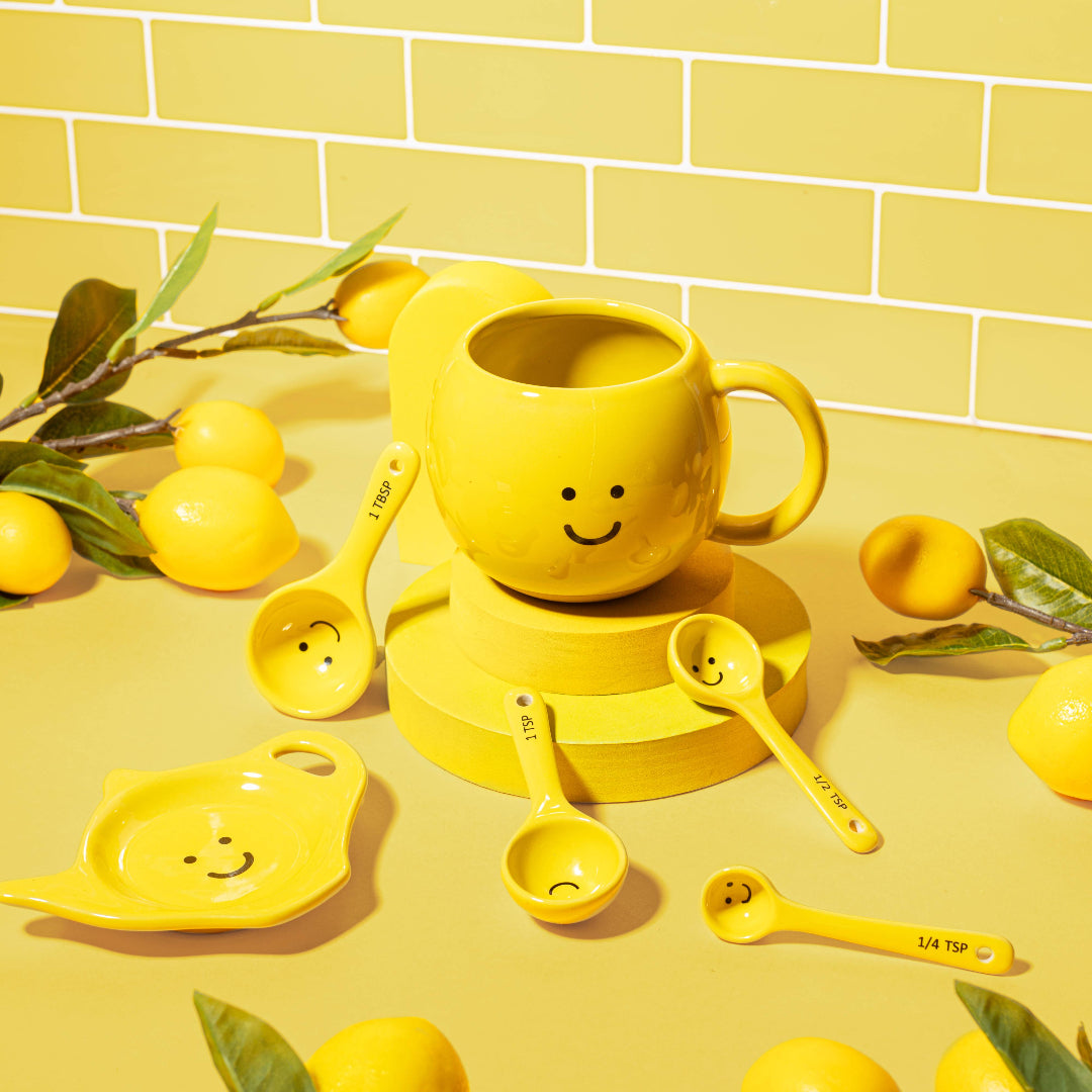 Taza amarilla con carita sonriente alrededor de otros objetos amarillos con caritas sonrientes. 