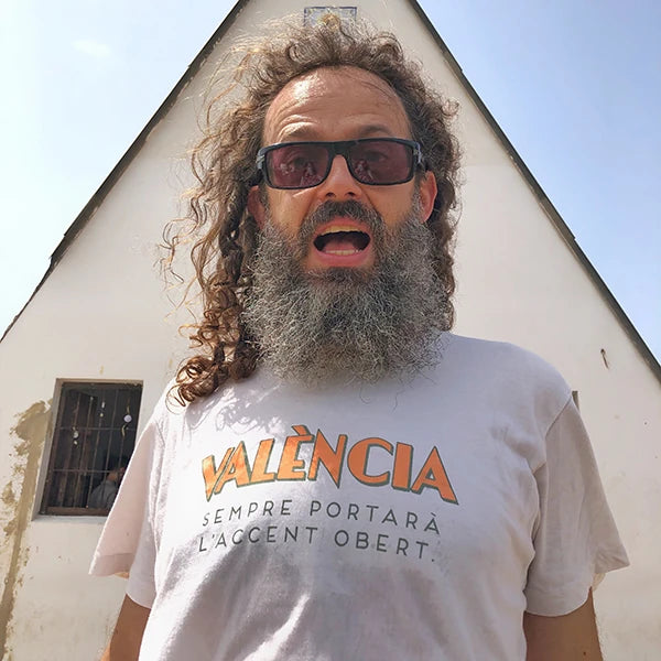 Home amb gafes de sol i samarreta reivindicativa en valencià amb la frase "València sempre portarà l'accent obert" de la dissenyadora Vir Palmera