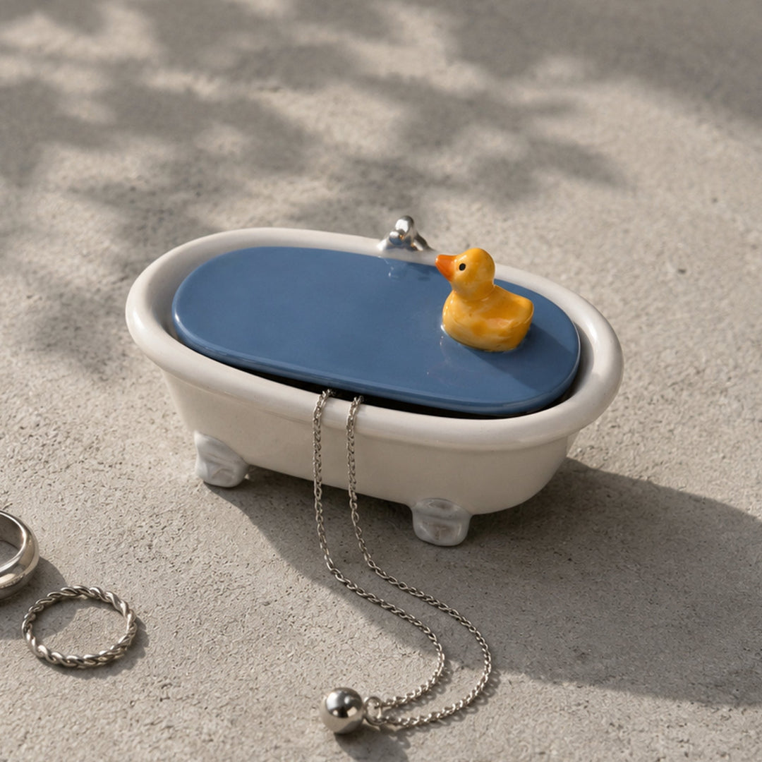 Joyero de cerámica con forma de bañera La tapa es el agua sobre la que flota un pato amarillo. soresale una cadena de plata