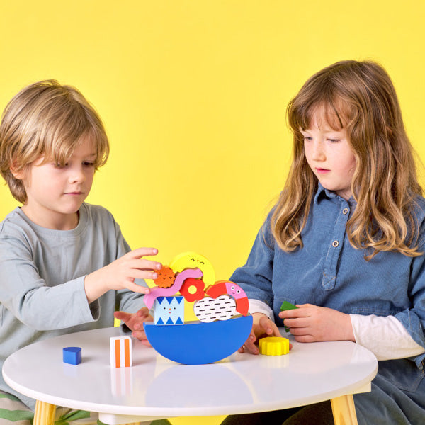 Un niño y una niña juegan con el juguete de equilibrio con piezas de madera de diferentes colores y formas