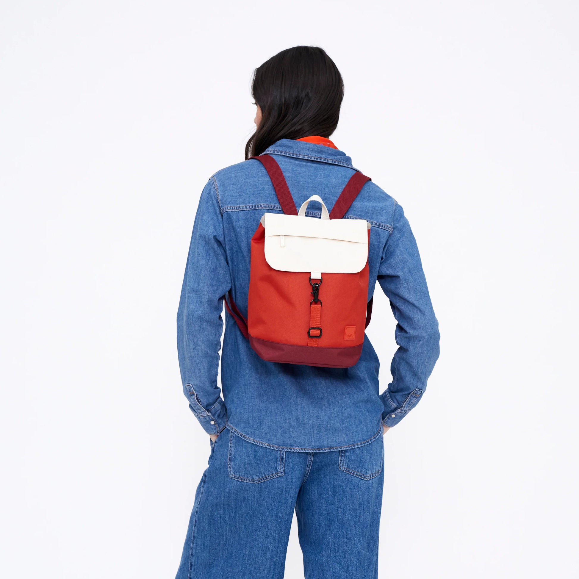 Mujer de espaldas vestida de vaquero con una mochila roja cereza y blanca de la marca Lefrik