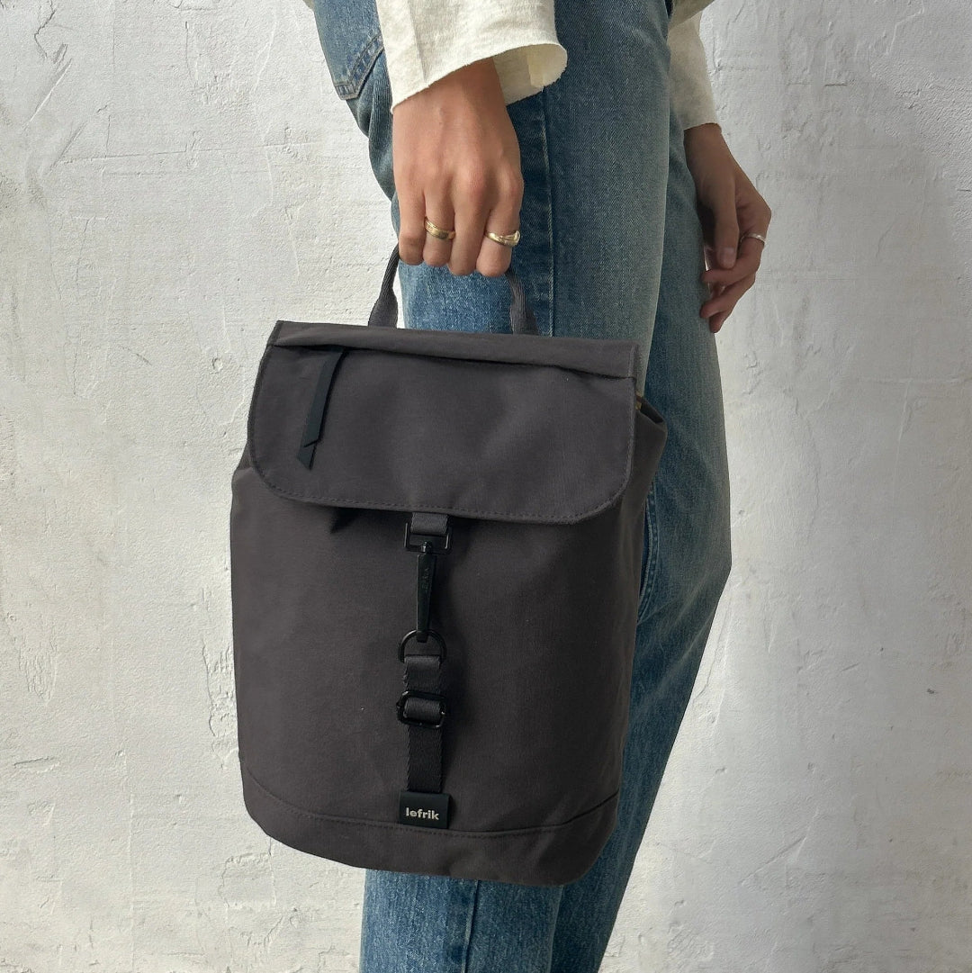 Mochila Kaut mini Arles Cemento de Lefrik en gris oscuro, sostenida de la mano por el asa superior.