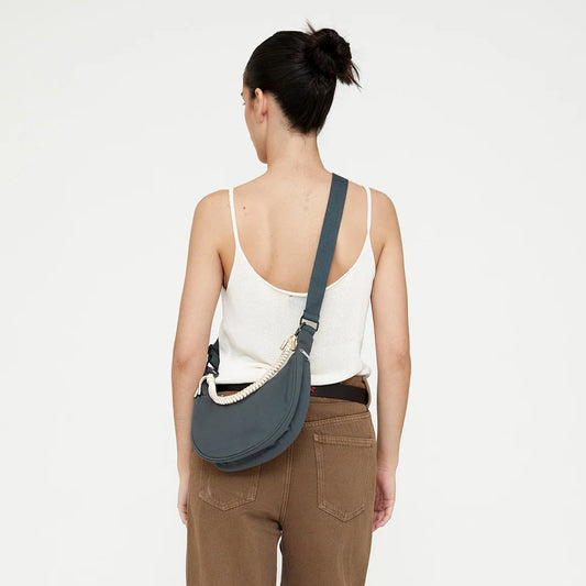 modelo de espaldas posando con el bolso lua de lefrik en color hoja de laurel azul con una correa trenzada unida a las asas en color blanco