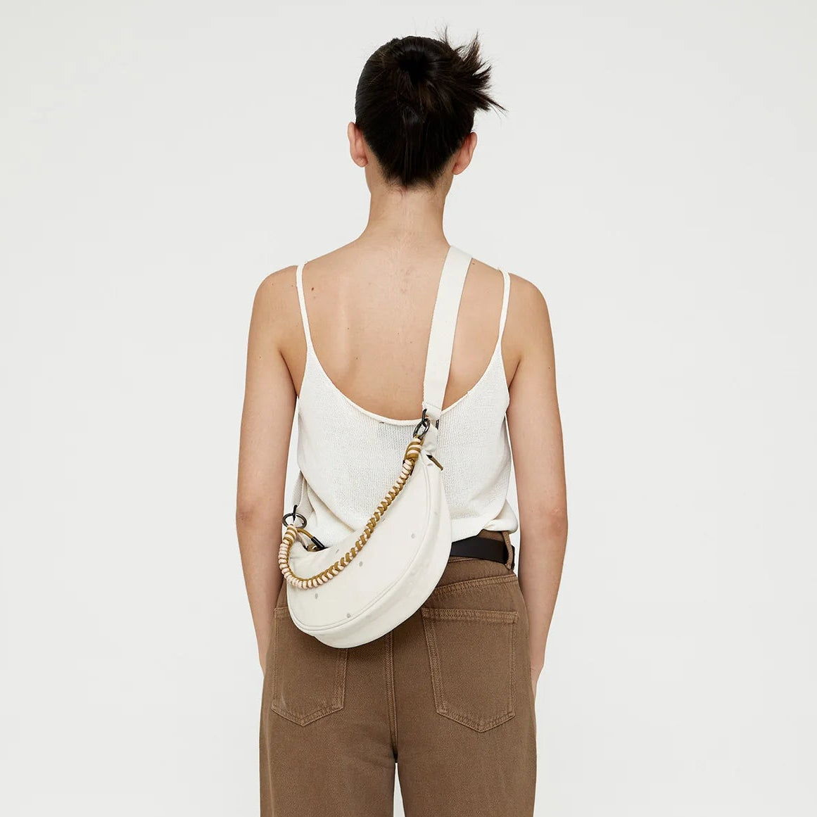 chica de espaldas con el bolso lua de lefrik en color blanco con puntos en crudo, con una correa cruzada en color blanco y beige, enganchada a las asas con dos aros metálicos