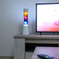 Lámpara de lava con estructura blanca y degradado de colores junto a un televisor