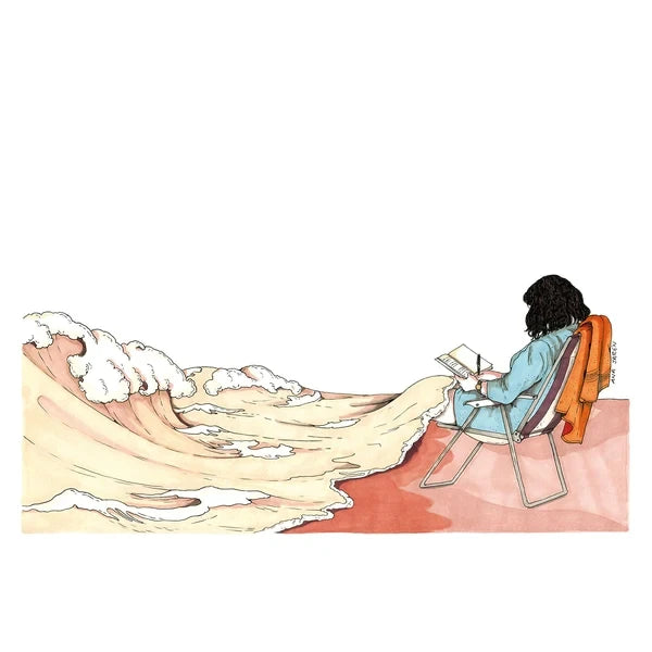 Una chica escribe en una libreta sentada en una silla en la playa mientras una ola blanca le arropa las rodillas como si fuera una manta