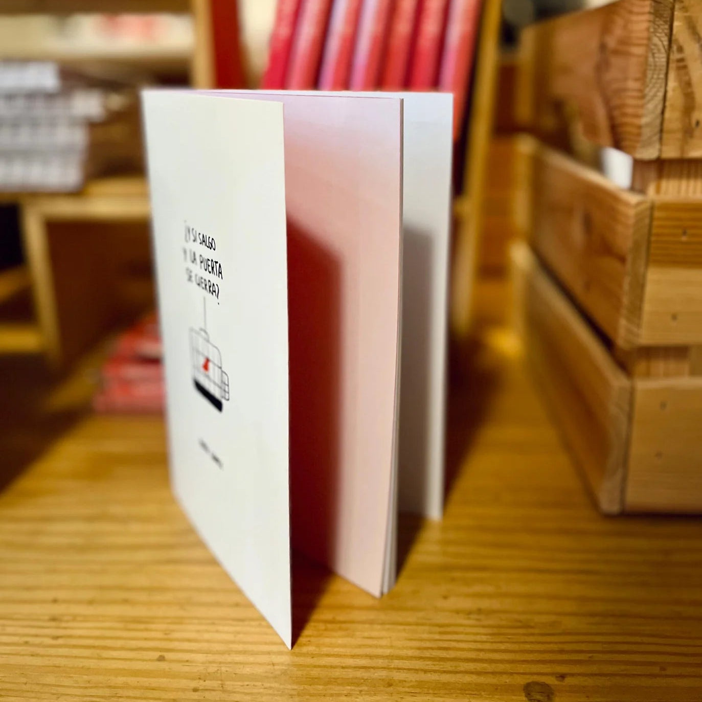 libreta con grapas de la marca voraz con un dibujo de un pájaro de color rojo en una jaula y con el texto ¿y si salgo y la puerta se cierra? puesta de pie y medio abierta