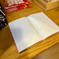 libreta con grapas de la marca voraz con un dibujo de un pájaro de color rojo en una jaula y con el texto ¿y si salgo y la puerta se cierra? abierta totalmente con páginas blancas en el interior