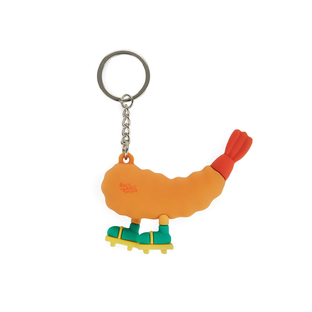 Parte trasera del llavero de una gamba naranja sonriente, de punta rojiza, con calcetines verdes y chanclas amarillas sobre fondo blanco. 