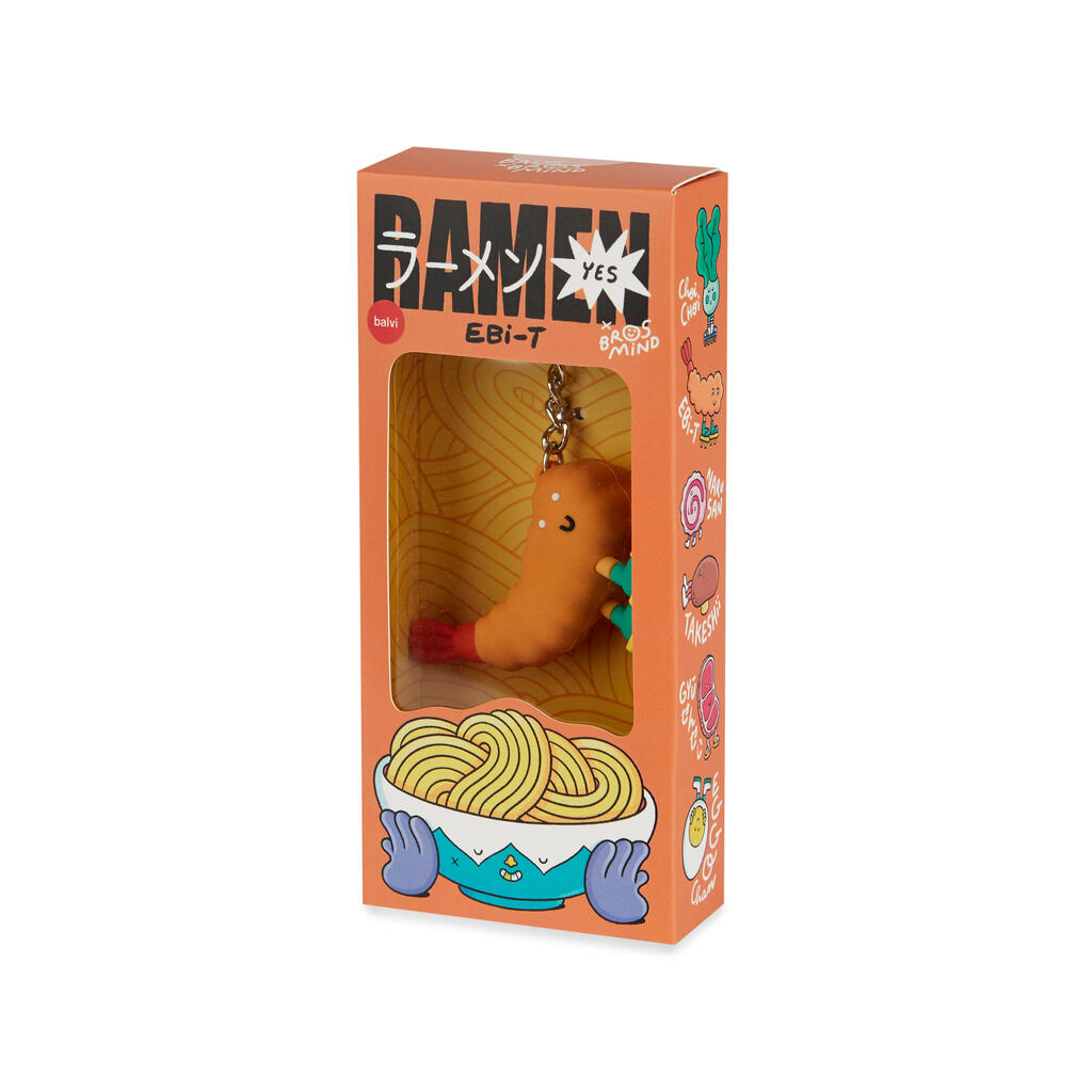 Caja naranja con detalles de dibujos de diferentes ingredientes del ramen, con letras japonesas y en el interior se ve la parte frontal del llavero de una gamba naranja sonriente, de punta rojiza, con calcetines verdes y chanclas amarillas sobre fondo blanco. 