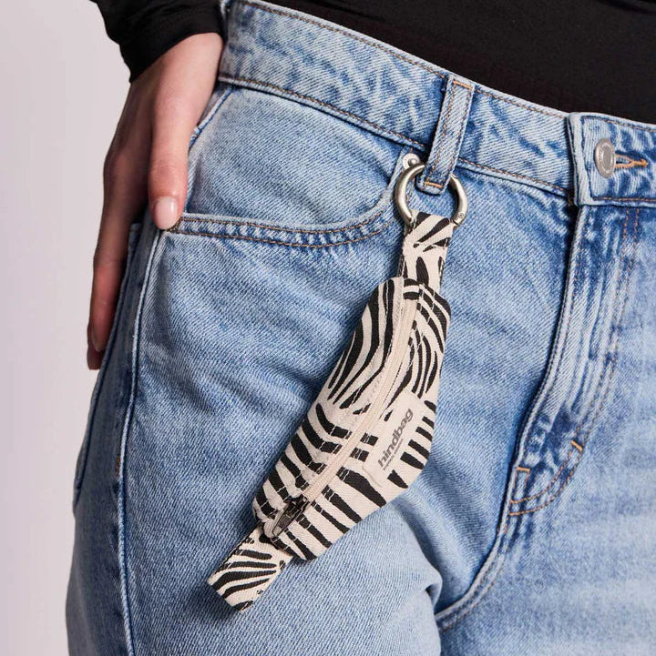 Llavero cebra color crema con forma de plátano enganchado a unos vaqueros. 