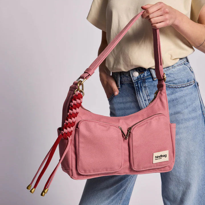 Llavero modelo Sammy de Hindbag en tonos rosas trenzado y con detalles metçalicos enganchado a un bolso de la misma marca agarrado por una persona. 