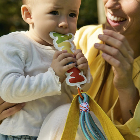 bebé en brazos de su madre chupando un llavero de bolso blandito con forma de la palabra mamá