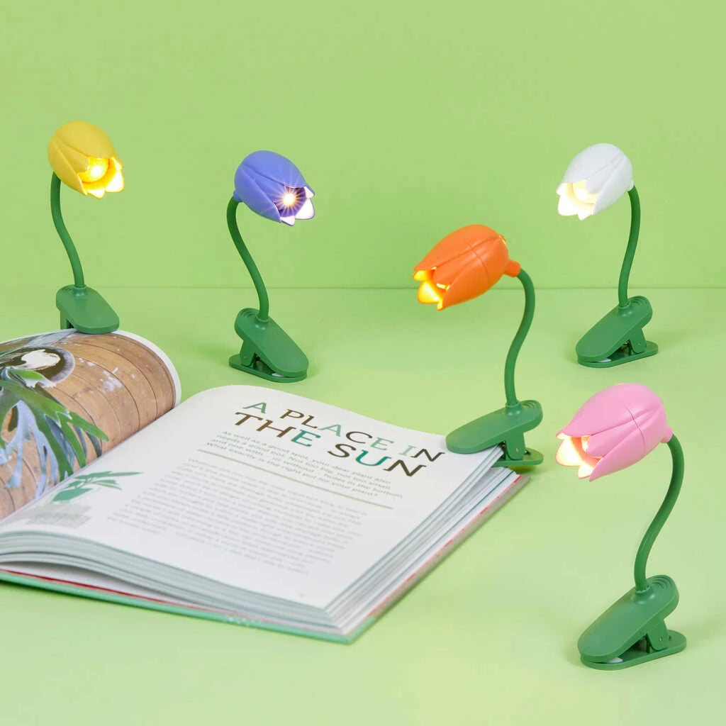 Lámparas de lectura con pinza y forma de tulipán de diferentes colores con un libro
