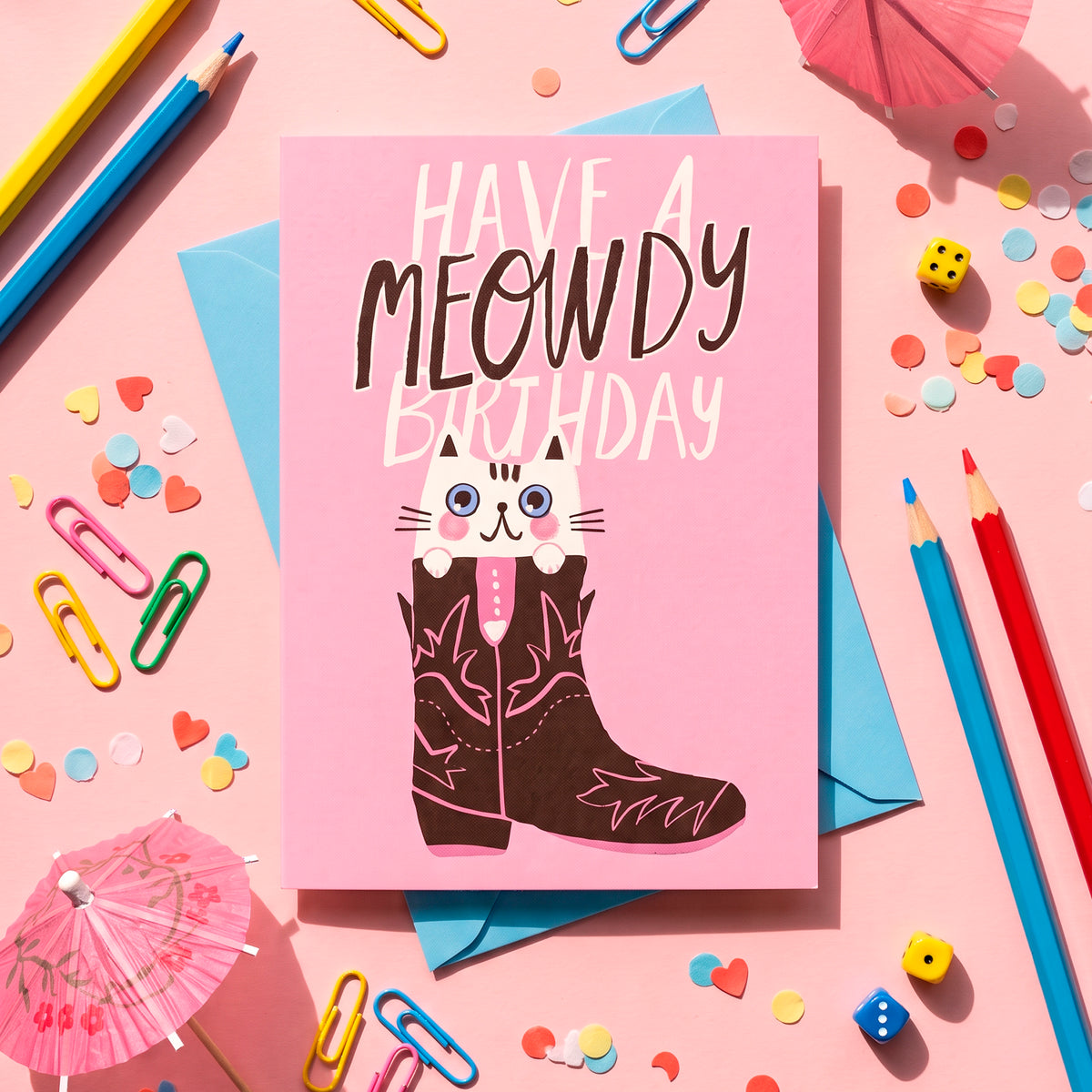 Minitarjeta Meowdy Birthday de Laura Ortiz, con un gato dentro de una bota vaquera sobre fondo rosa, entre confeti y lápices.
