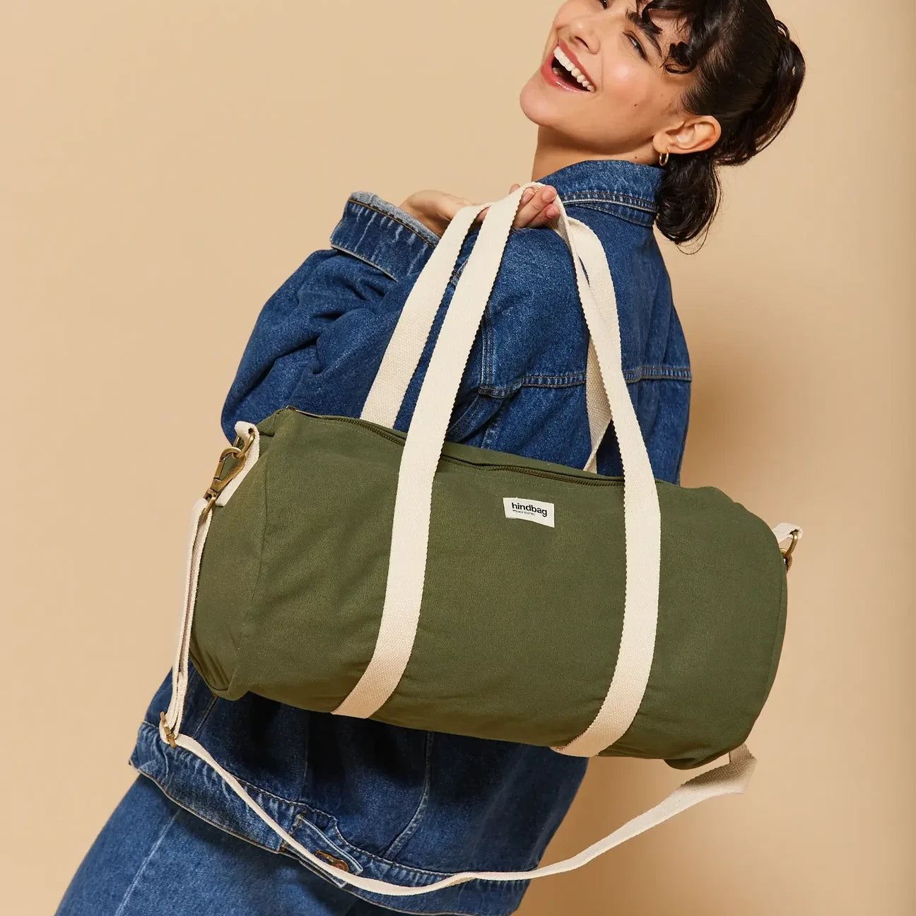 Mujer vestida de vaquero con la bolsa de viaje pequeña de la marca francesa Hindbag en verde militar con correas beige 