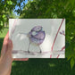 Mini print con ilustración de un pájaro morado de Marialu Gili fotografiada en un jardín