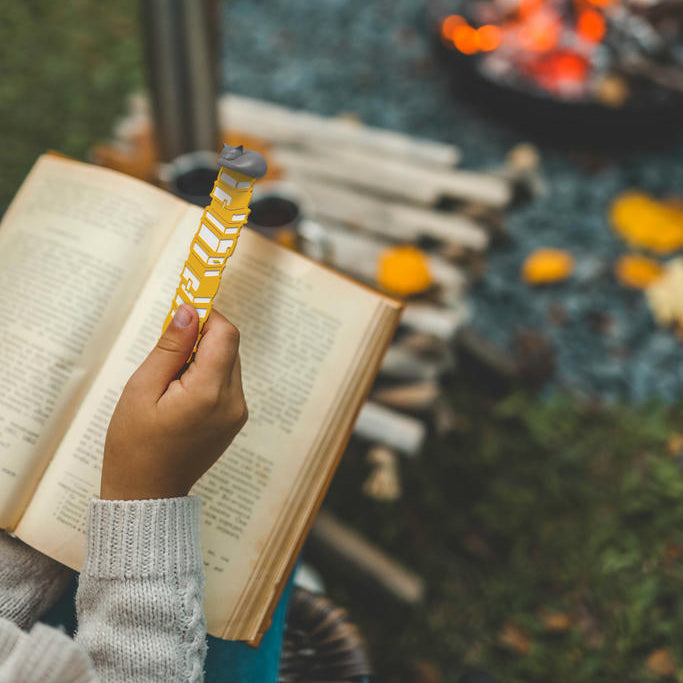 Una persona sujeta un marcapáginas con un gatito acurrucado sobre una pila de libros delante de un libro