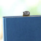 En un libro azul cerrado se asoma un marcapáginas 3D de un libro amarillo con un gato gris dormido encima
