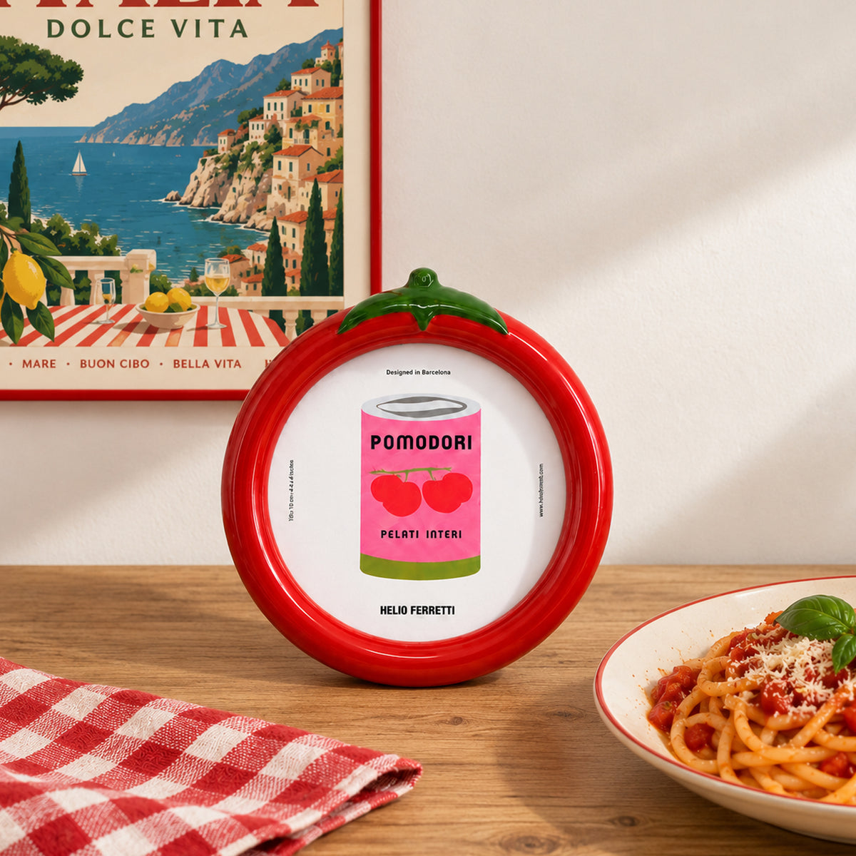 «Marco de fotos Tomate de Helio Ferretti, rojo con hojas verdes, sobre una mesa junto a un plato de pasta.»