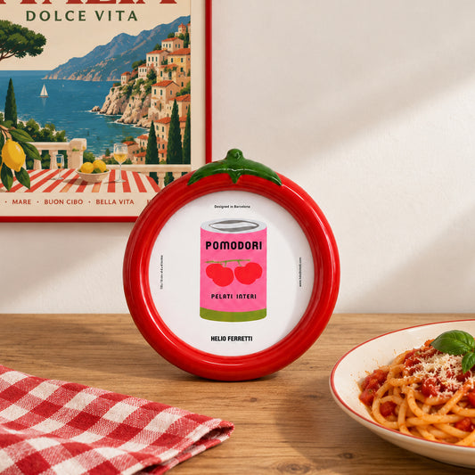 «Marco de fotos Tomate de Helio Ferretti, rojo con hojas verdes, sobre una mesa junto a un plato de pasta.»