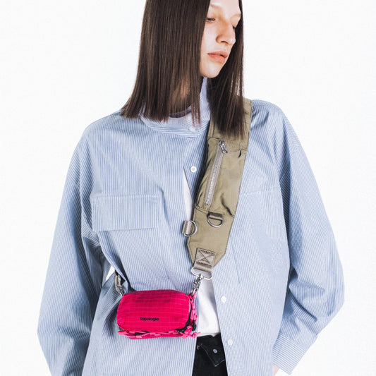 Chica con el bolso Mini Bottle Sacoche de Topologie en color fucsia colgado de una correa de hombro