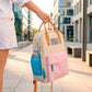 Mujer llevando una mochila crema y pastel pequeña con bolsillos y la frase "Born to be cute" bordada agarrada por las asas y con una botella de agua en el bolsillo de malla lateral