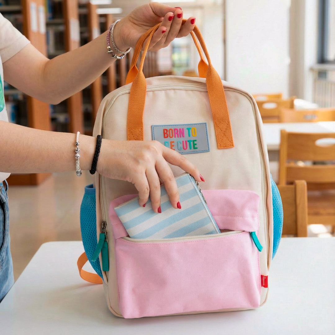 Mujer en la biblioteca metiendo una cartera en la mochila crema y pastel pequeña con bolsillos y la frase "Born to be cute" bordada