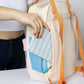 Mujer metiendo una cartera en el bolsillo antirrobo con cremallera de la mochila crema y pastel pequeña con bolsillos y la frase "Born to be cute" bordada