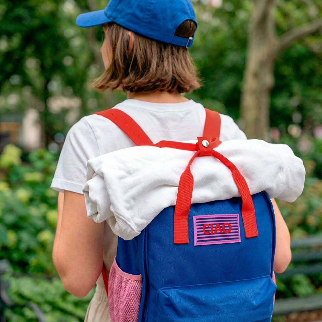 Mujer de espaldas con una mochila azul marino y roja con una sudadera enrollada