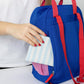 Mujer metiendo una cartera en el bolsillo trasero antirrobo de la mochila pequeña azul y roja con el mensaje ciao