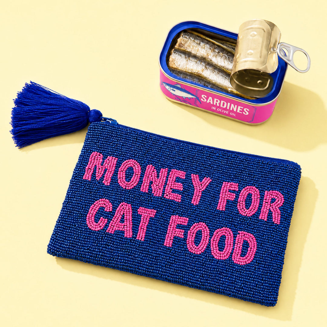Monedero grande hecho de cuentas azul marino con borla en la cremallera y el mensaje MONEY FOR CAT FOOD en cuentas rosas al lado de una lata de sardinas